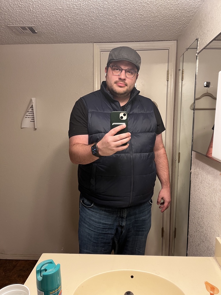 Shawn Lopp taking an iPhone mirror photo in a flat cap and vest