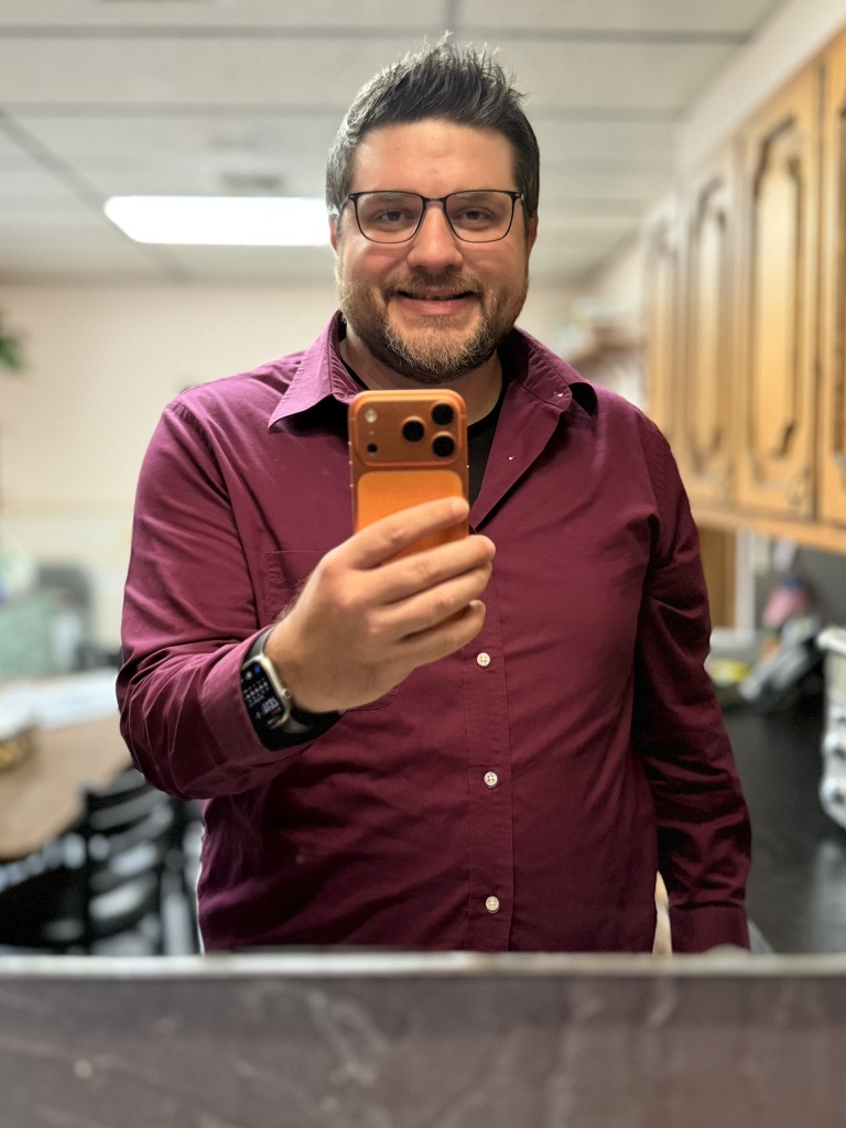 Shawn Lopp smiling with an orange iPhone in a mirror photo